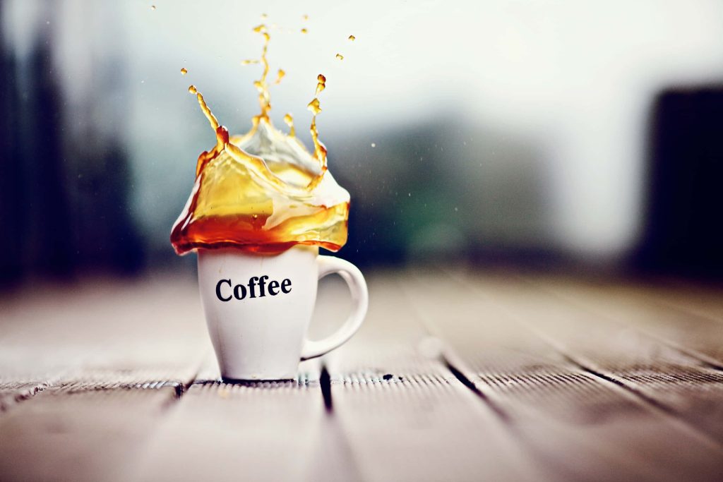 White coffee mug with dynamic brown liquid splash on blurred wooden background wallpaper