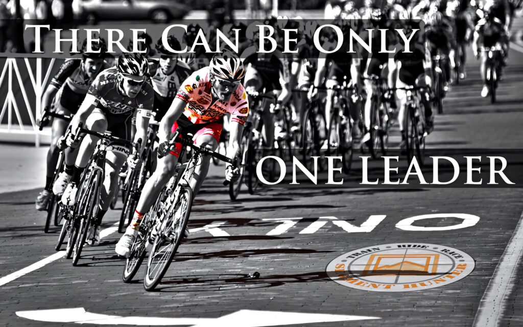 Competitive cyclists racing on sunlit city street with lead rider highlighted in dynamic curve Wallpaper