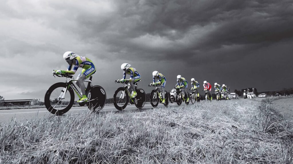 Cyclists in blue and green racing gear speeding on rural road with stormy sky background Wallpaper