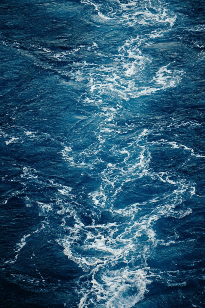 High resolution ocean wallpaper showing deep blue swirling waves with white foam texture