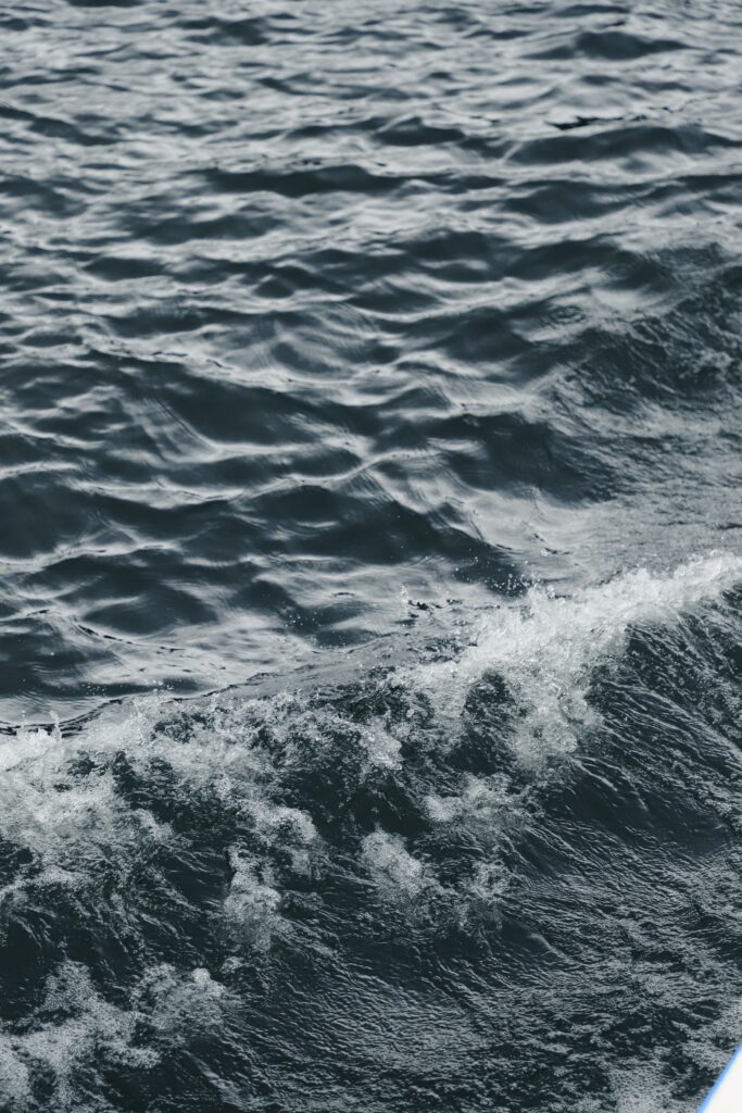 Dynamic deep blue sea waves with textured water sprays reflecting natural light background Wallpaper
