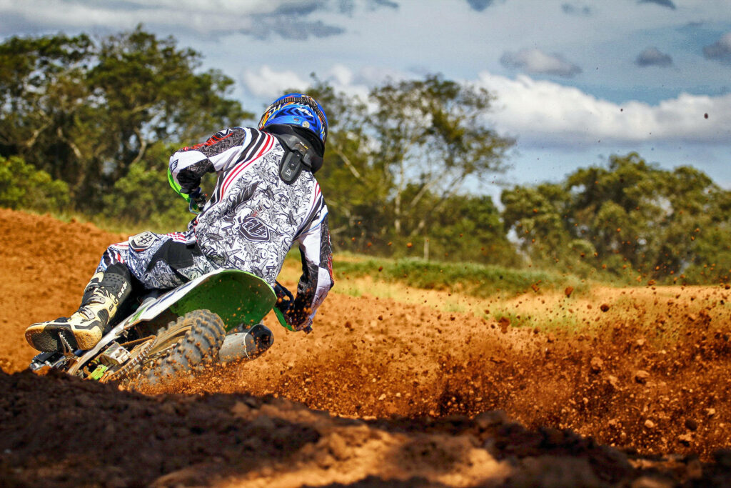 Dirt bike rider speeding on rugged track kicking up brown dirt with vivid motion blur background Wallpaper