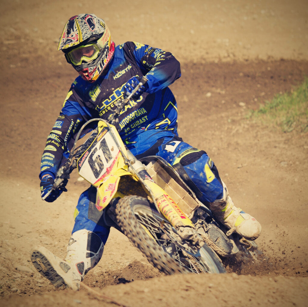 Motocross rider in blue and yellow gear racing on dusty dirt track capturing speed thrill Wallpaper