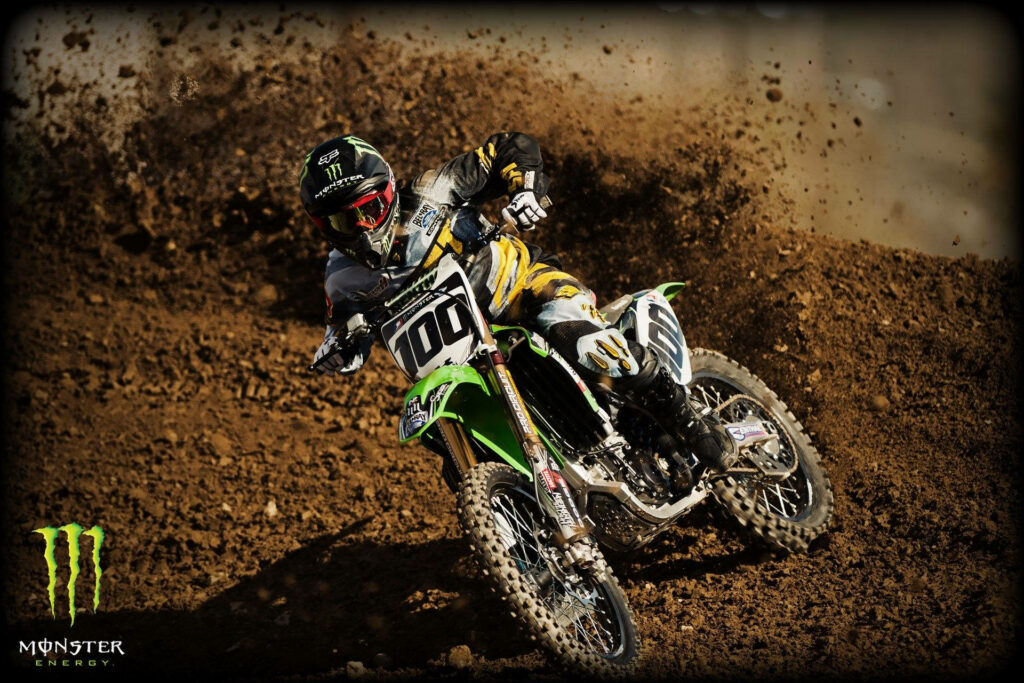 Dirt bike rider in racing gear kicking up dirt on rugged motocross track with Monster Energy logo Wallpaper