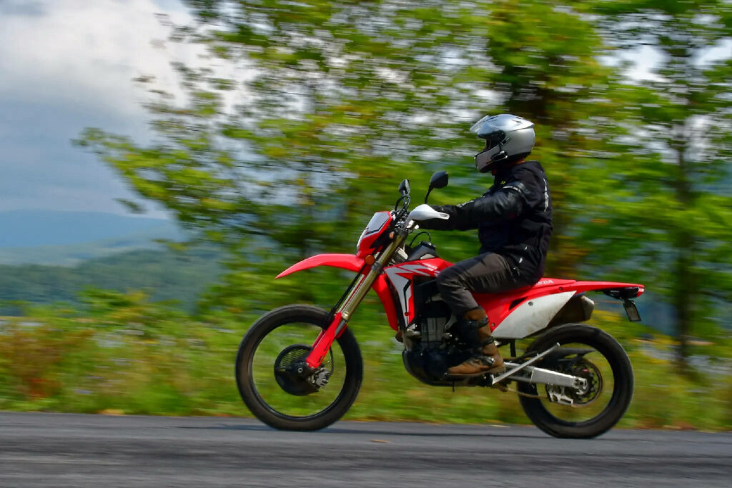 Dirt bike rider speeding on red off-road motorcycle with green trees and motion blur background Wallpaper