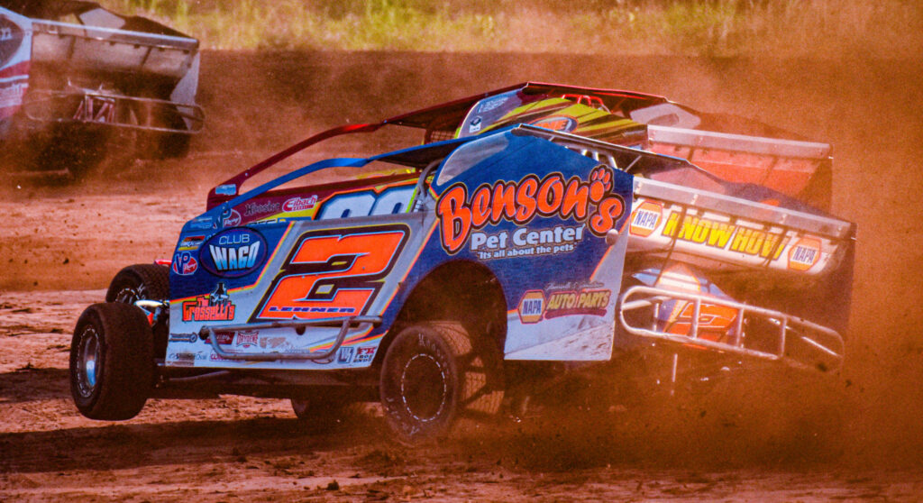 Orange and blue dirt car racing on dusty track with flying debris and blurred background motion Wallpaper