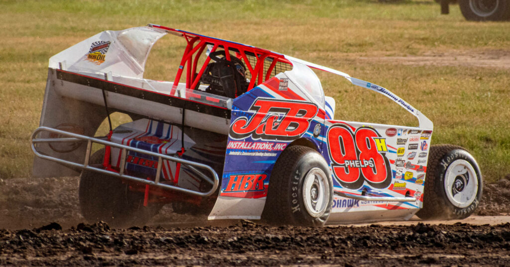Red white and blue dirt race car speeding on rugged track kicking up dust with motion blur background Wallpaper