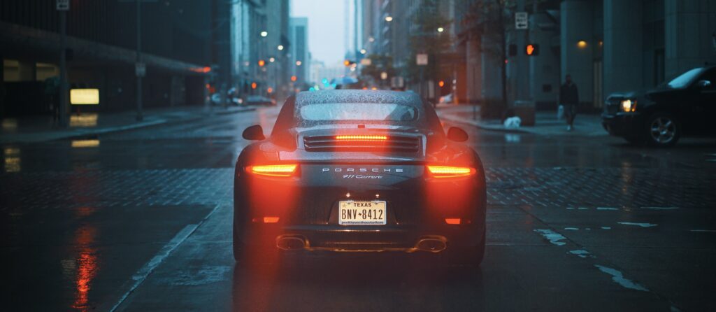 Evening Cruise: Sleek Car Back View on Wet City Street Wallpaper