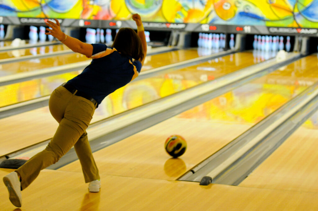 Female bowler mid-throw in vibrant bowling alley with colorful murals and polished lanes wallpaper