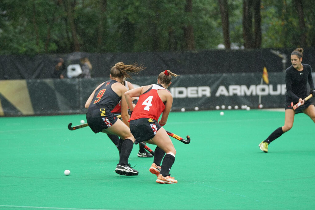 Dynamic Female Field Hockey Athletes Wallpaper on Vibrant Green Field