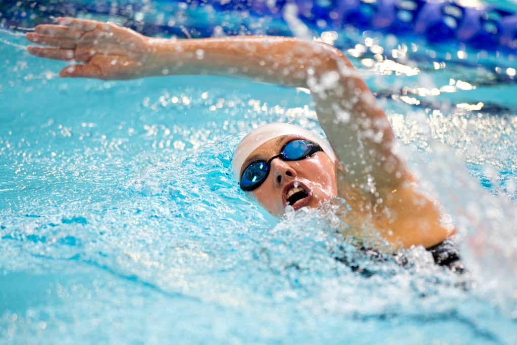 Female Olympic swimmer freestyle stroke in bright blue water with dynamic splashes wallpaper