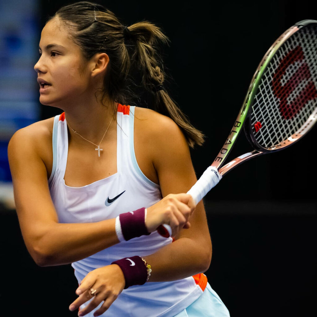 Female tennis player mid-swing in white and orange sportswear with intense focus on dark background Wallpaper