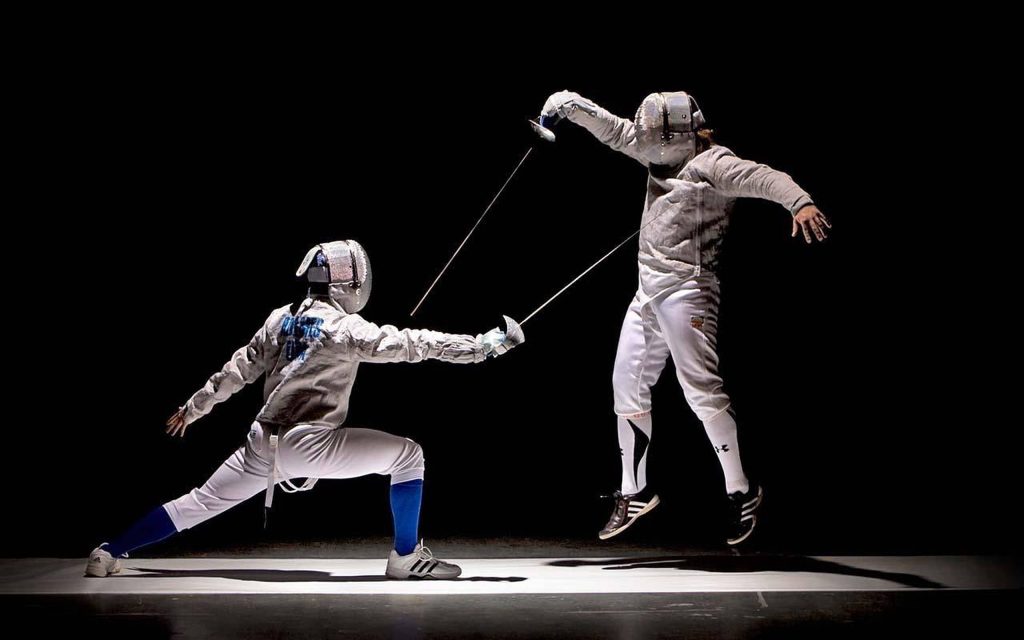 Two fencers in white gear lunging and leaping against black background intense fencing match Wallpaper
