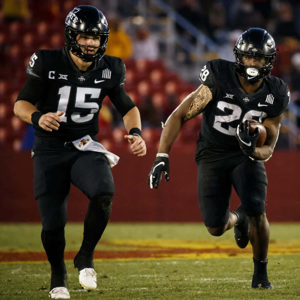 Dynamic football wallpaper of quarterback handing off to Breece Hall in black uniforms on field