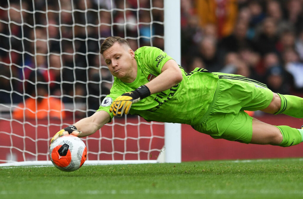 Goalkeeper in green kit diving to save soccer ball near net dynamic football action wallpaper