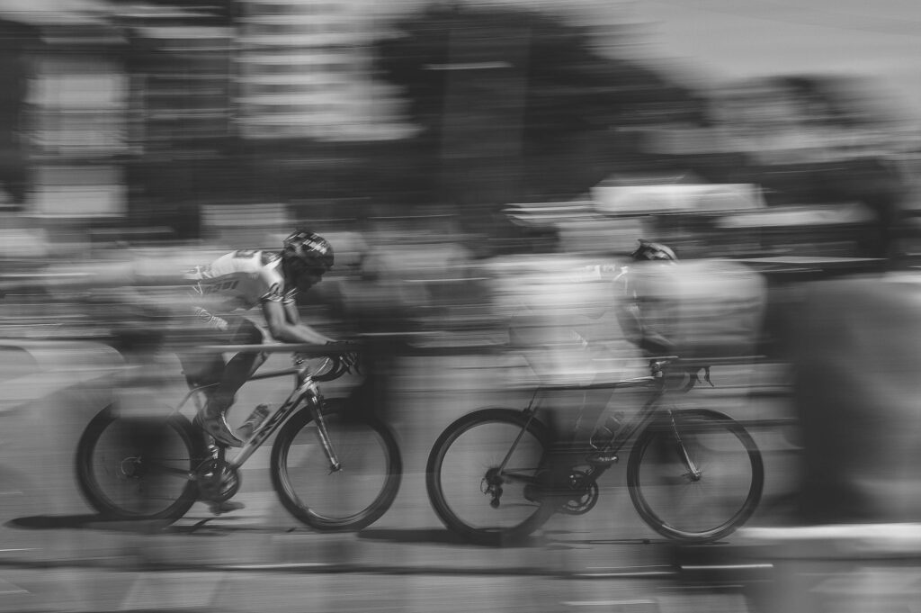 Grayscale photo of two cyclists racing fast with blurred motion against soft urban background wallpaper