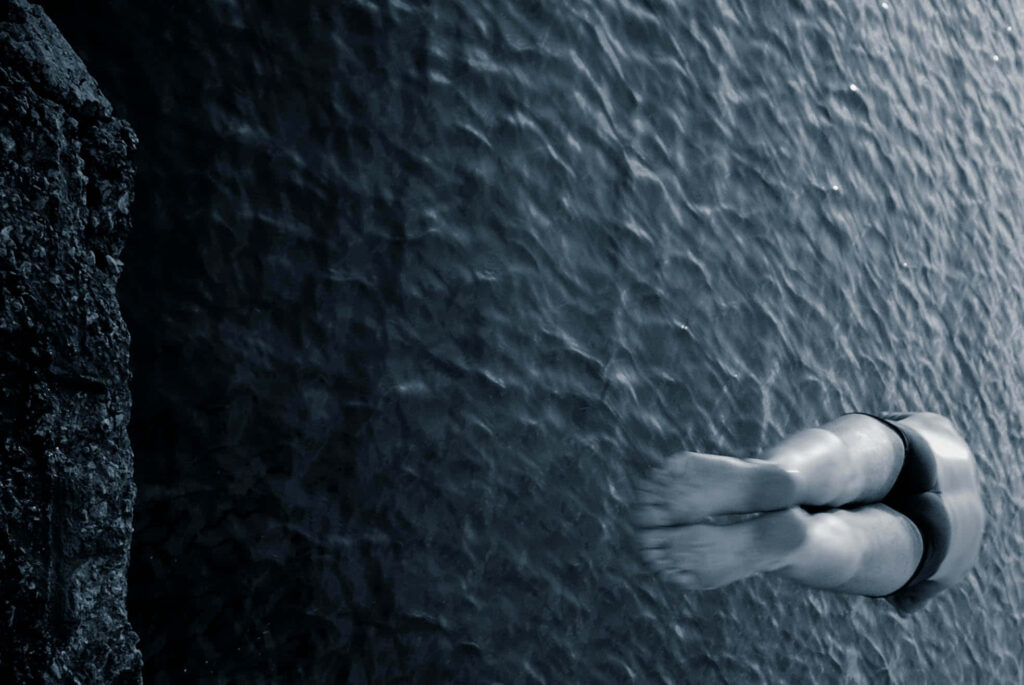 Greyscale wallpaper of male diver with outstretched feet diving into rippling water motion background