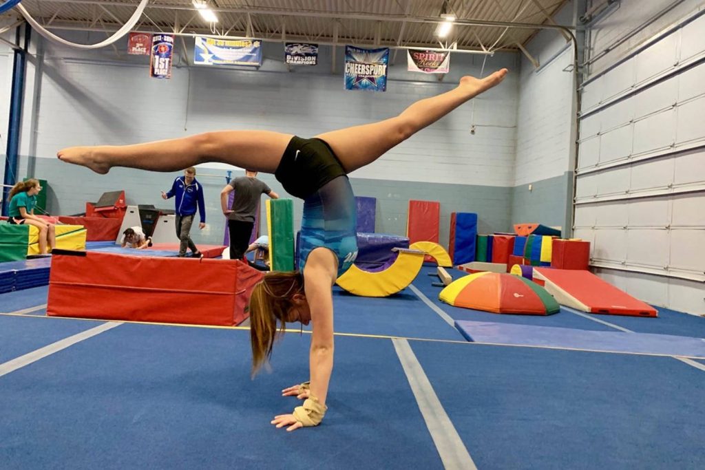 Young gymnast in vibrant gym performs perfect handstand split showcasing balance and skill Wallpaper