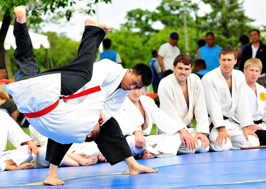 Hapkido outdoor class with martial artist throwing opponent on blue mat surrounded by students Wallpaper