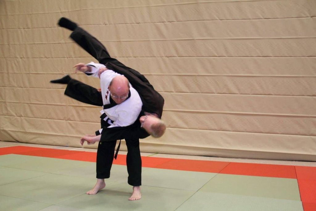 Dynamic Hapkido shoulder throw by martial artist in white uniform on dojang mat background Wallpaper
