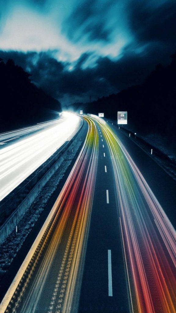 Long-exposure iPhone wallpaper with vibrant white and red light trails on dark highway night