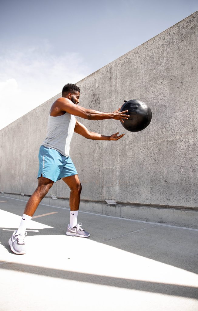 Man doing medicine ball workout exercise against concrete wall in bright daylight fitness photo Wallpaper