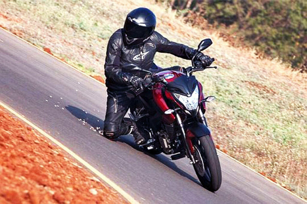 Vibrant NS 200 Rider Swerving on Scenic Road - Dynamic Wallpaper