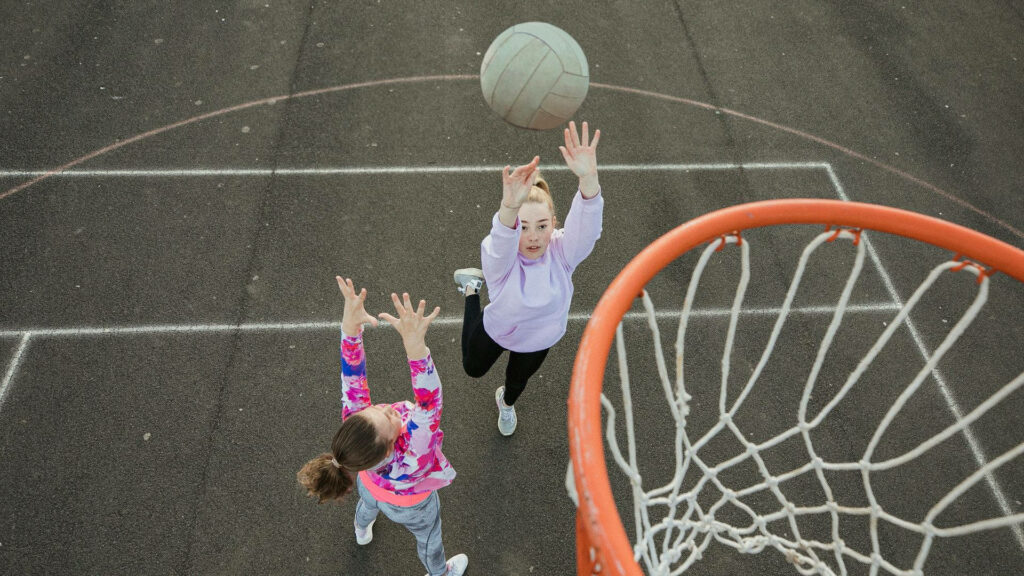 Dynamic Netball Wallpaper: Two Girls in Action on Outdoor Court