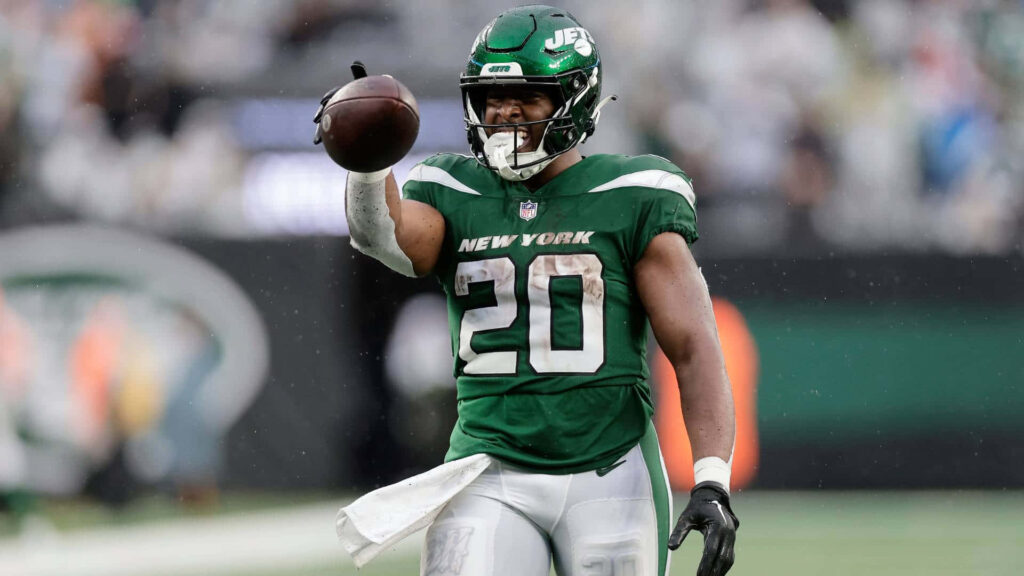 Breece Hall in green white Jets uniform holding football on field intense action wallpaper