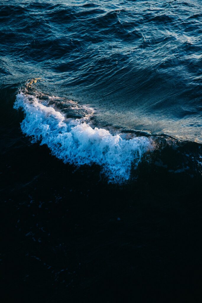 Powerful ocean wave wallpaper with deep blue turquoise tones and white foam under storm light