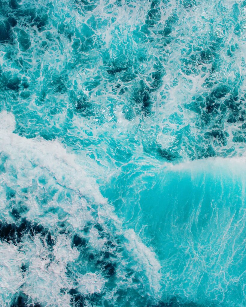 Aerial view of ocean waves crashing with white foam on deep blue and turquoise water wallpaper
