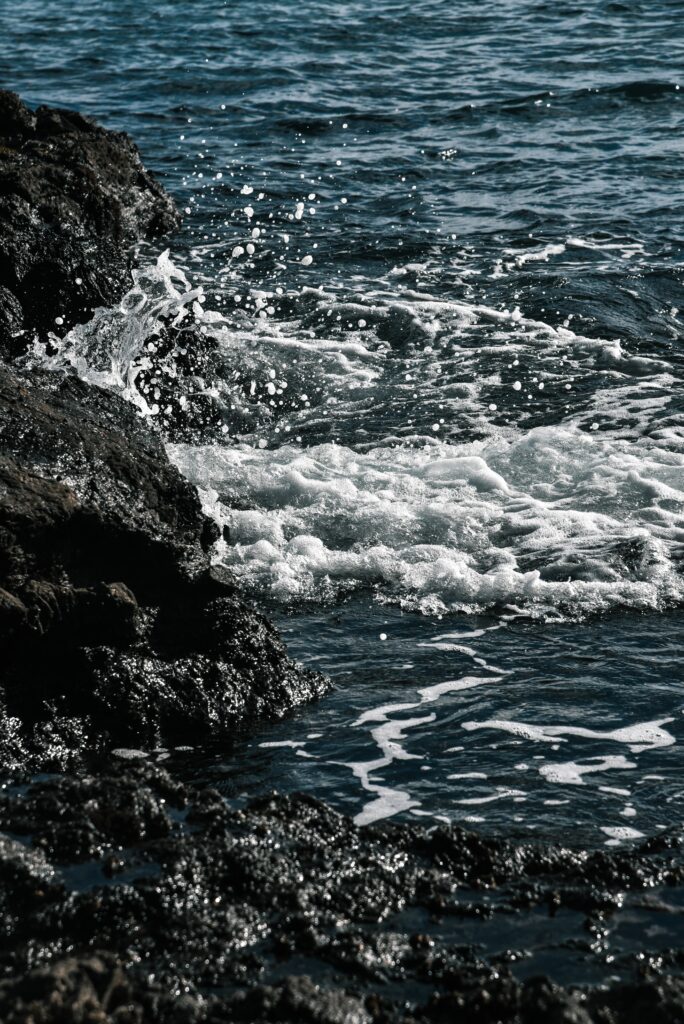 Waves crashing on dark coastal rocks with white spray above deep blue ocean water wallpaper