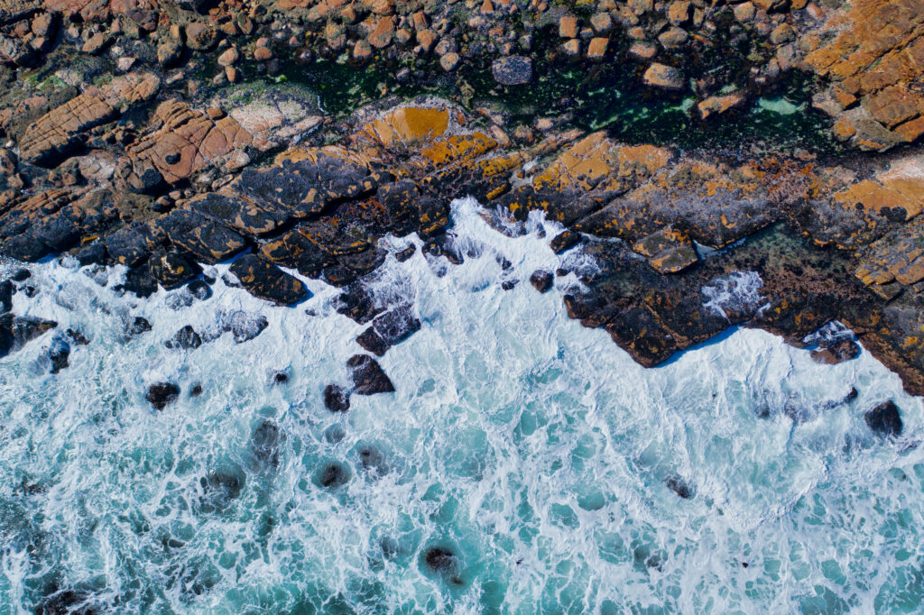 Ocean waves crashing on rugged rocky shore with blue white tides creating vibrant coastal scene Wallpaper