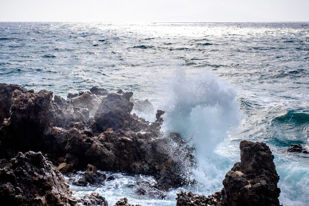 Dynamic waves crashing on rugged rocks under bright sky showcasing powerful coastal beauty Wallpaper
