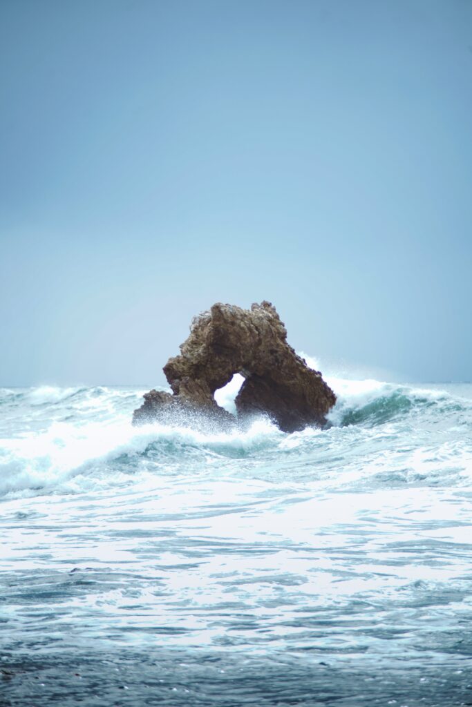 Waves crashing on rugged rocks with ocean spray under cloudy sky seaside nature wallpaper background