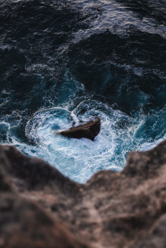 Rugged coastal rocks with swirling sea foam and deep blue waves crashing powerfully shore Wallpaper