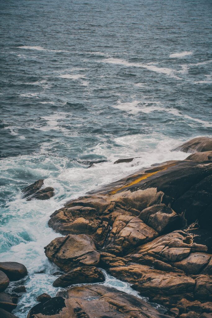 Powerful waves crash rugged stony shoreline white foam deep blue turquoise water coastal energy Wallpaper