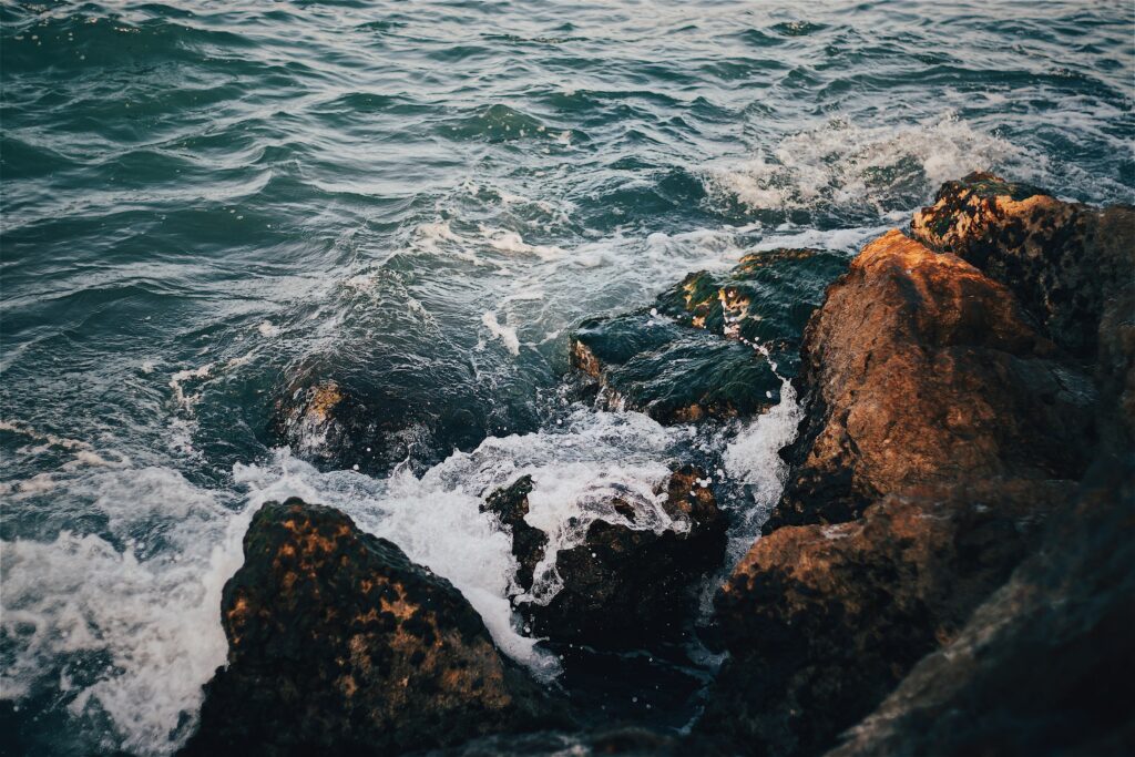 Dynamic ocean waves crash on textured rugged rocks under warm light vibrant sea wallpaper background