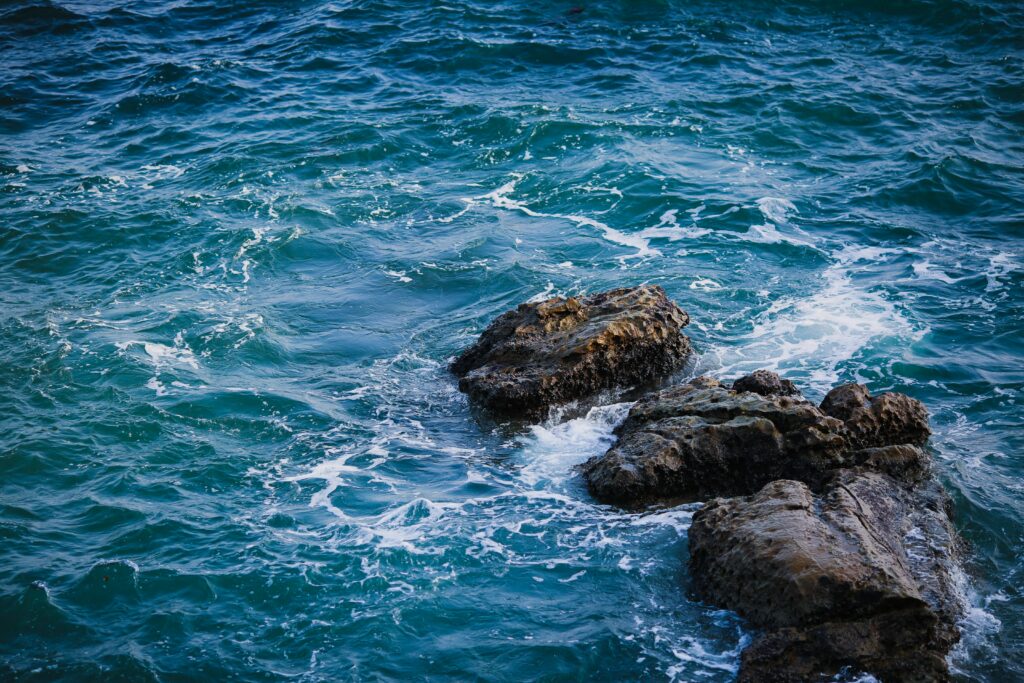 Dynamic sea waves crashing on rugged stones with deep blue and turquoise tones wallpaper background