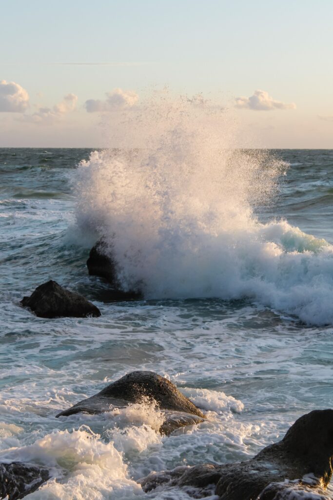 Ocean waves crashing on rugged stones with white spray lit by golden evening light wallpaper