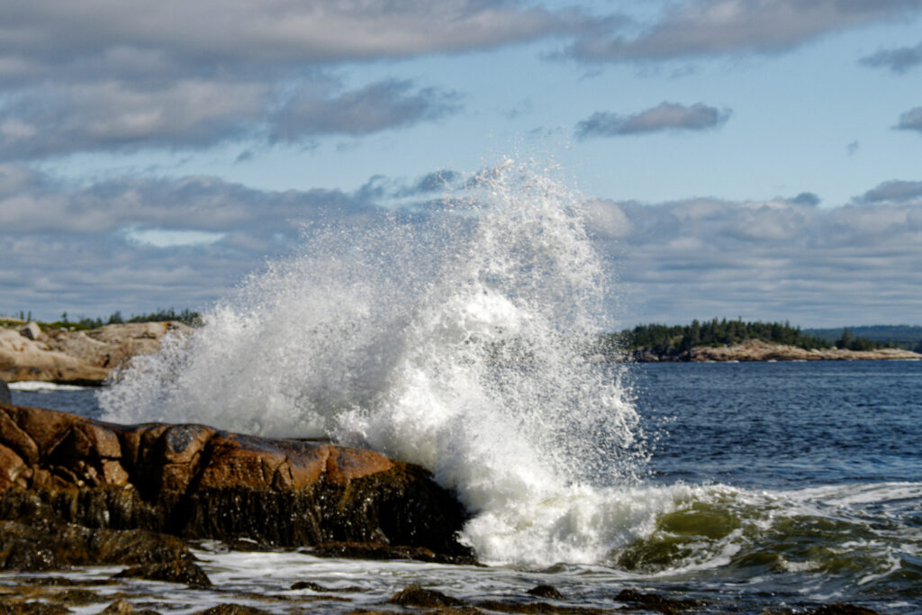 Dynamic ocean waves crash against rugged stones with white foam under textured cloudy sky wallpaper