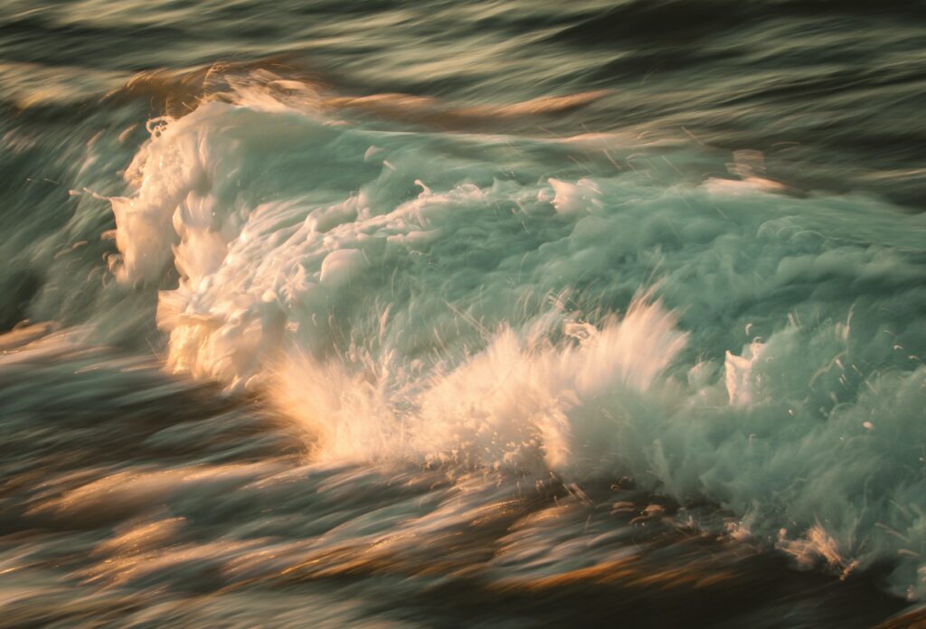 Dynamic ocean waves with teal and gold hues splashing powerfully in a vibrant natural wallpaper background