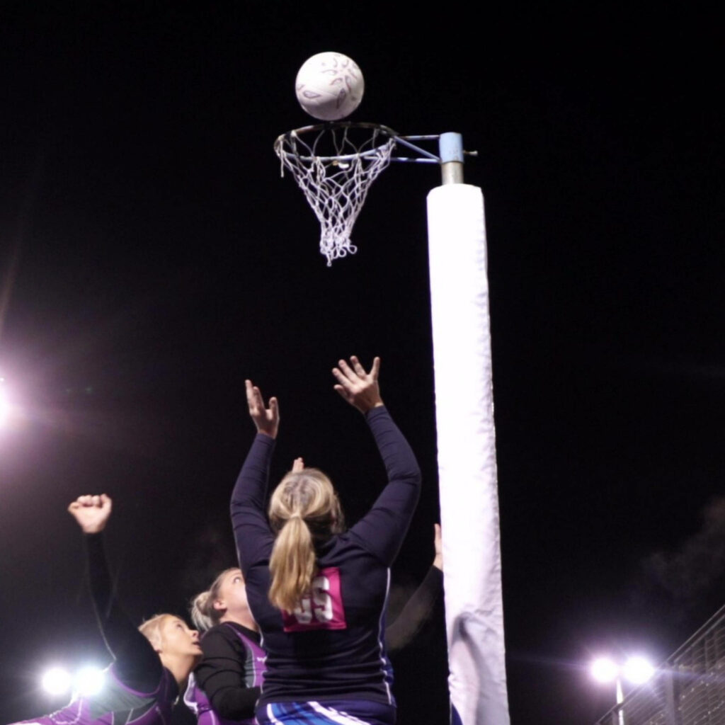 Dynamic Netball Game Wallpaper: Girls in Action Under Stadium Lights