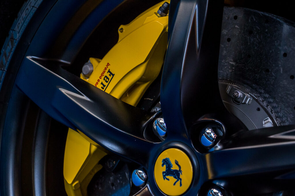 Dynamically Bold: Captivating Closeup of Red Ferrari Wheel with Radiant Golden Spokes on Sleek Black Canvas Wallpaper