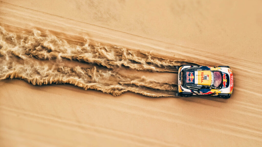Aerial view of a racing car speeding on sandy terrain kicking up dust trails wallpaper background
