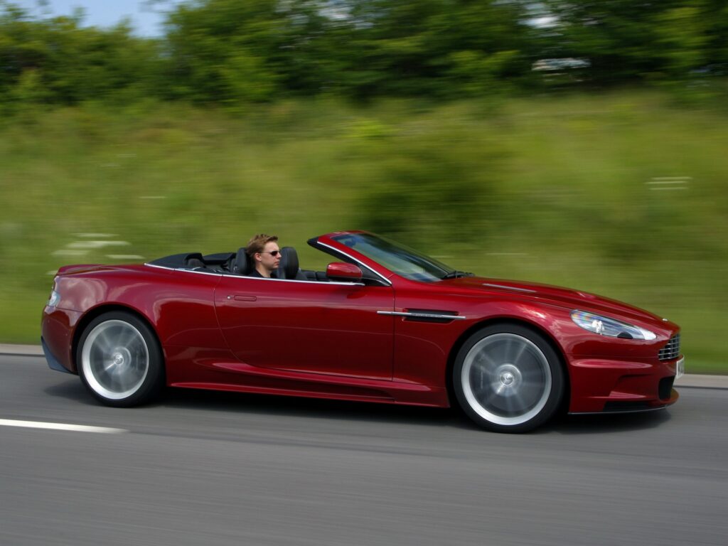 Sleek Red 2009 Aston Martin DBS in Lush Nature Background Wallpaper