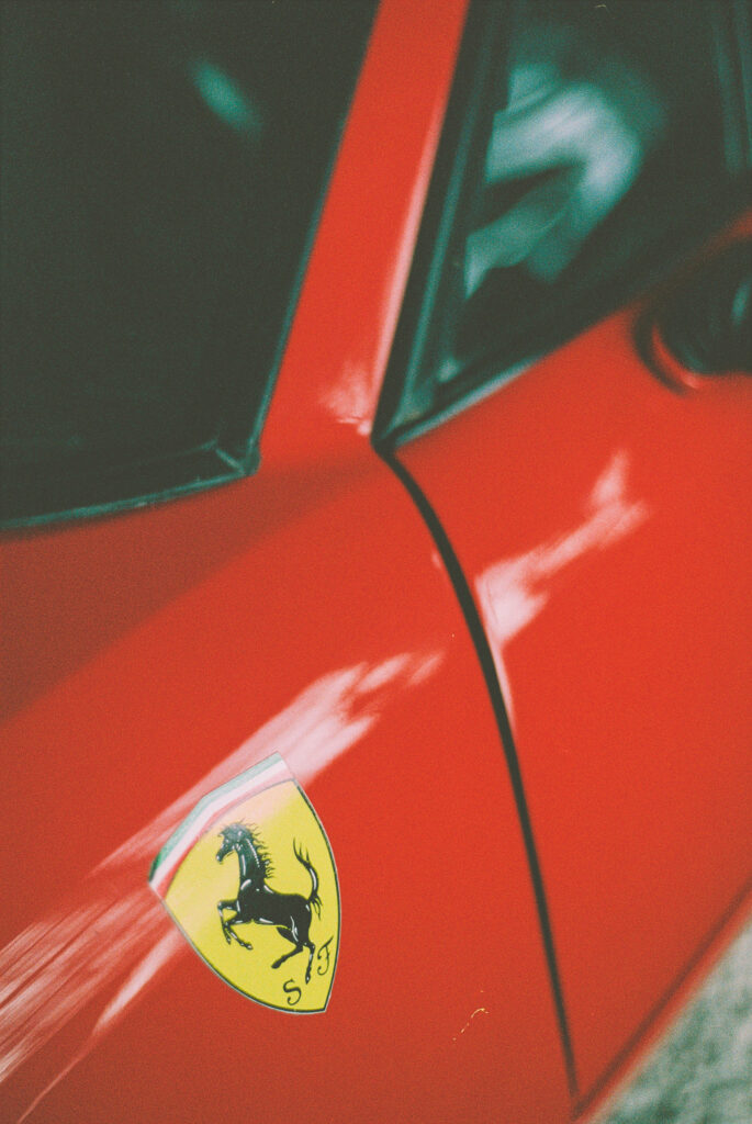 Vibrant Red Sports Car: Striking Close-Up of Left Panel with Yellow Ferrari Sticker Logo and Iconic Black Prancing Horse Wallpaper