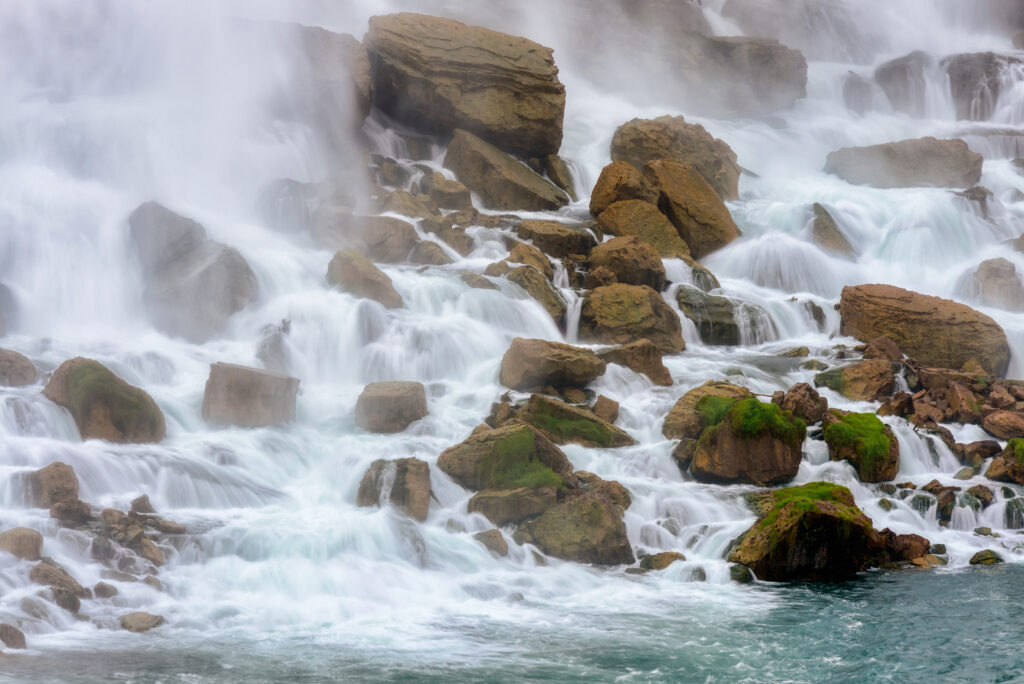 Dynamic river flowing over brown stones with green moss and misty white water spray wallpaper