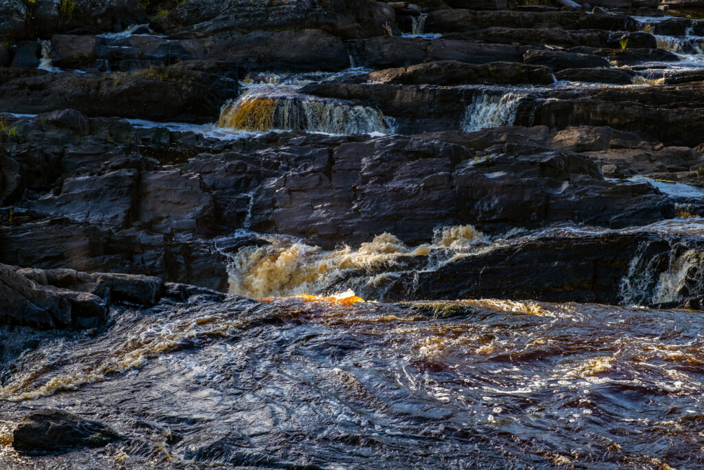 Dynamic river cascading over rugged rocks with light reflecting on flowing textured water wallpaper