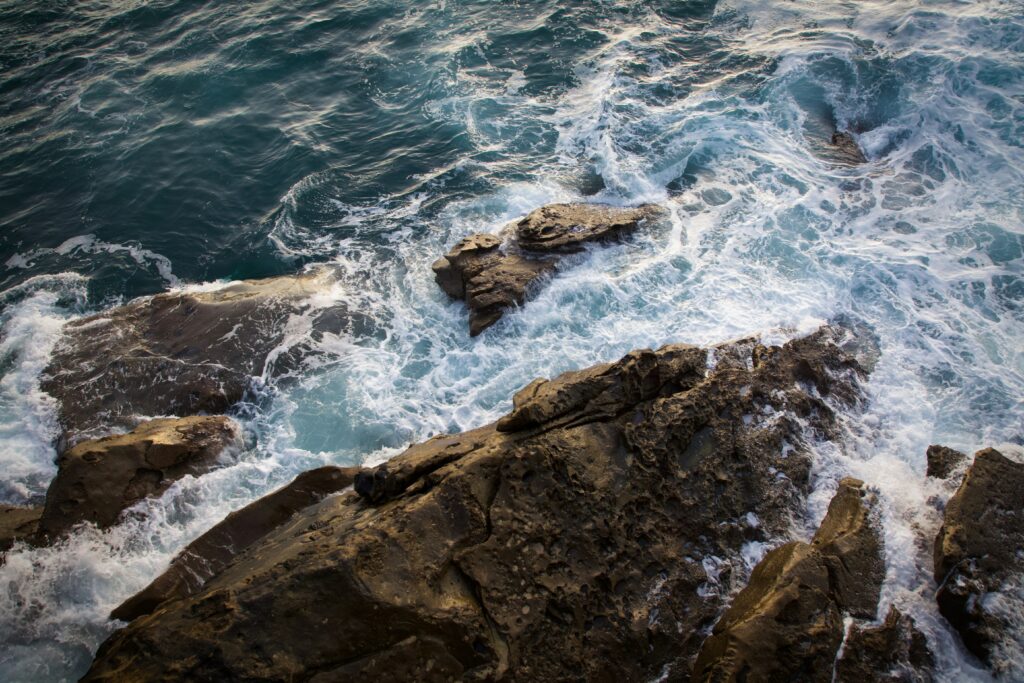 Vibrant wallpaper of foamy waves crashing on rugged coastal rocks with deep blue sea textures